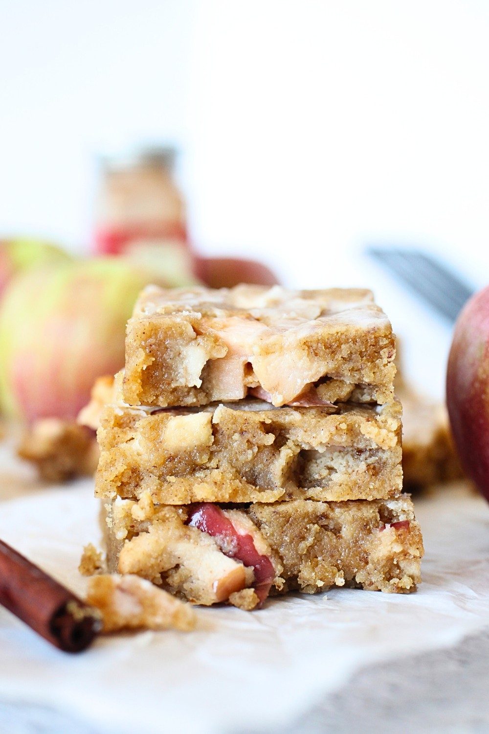 front view of keto apple fritter bars stacked on top of each other with apples and cinnamon sticks in the background