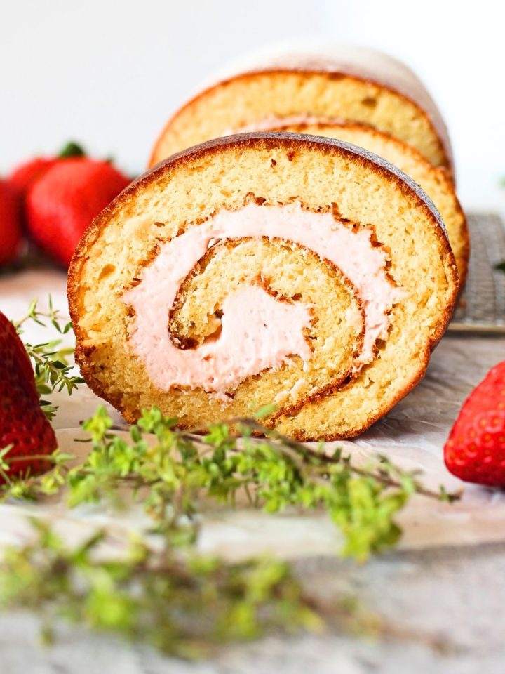 front view of keto vanilla roll cake with strawberry filling with strawberries scattered about